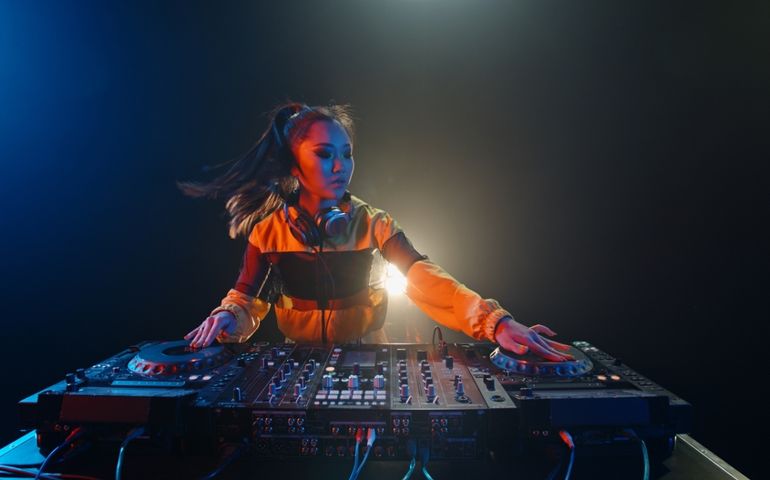 Cool female asian dj is working in a nightclub, standing at turntables, creating a dance music set - nightlife concept
