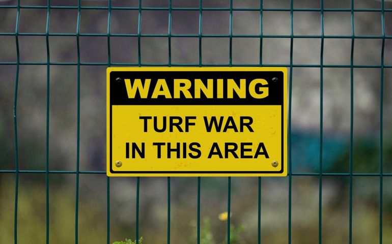 Red an white warning sign on a fence stating in "Warning - Turf war in this area" with a blank space underneath.