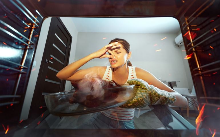 Young woman cooking dinner at home, preparing baked chicken. Overcooked meat. Covering nose in bad smell. View from oven. Concept of culinary, emotions, household, hobby, taste, lifestyle