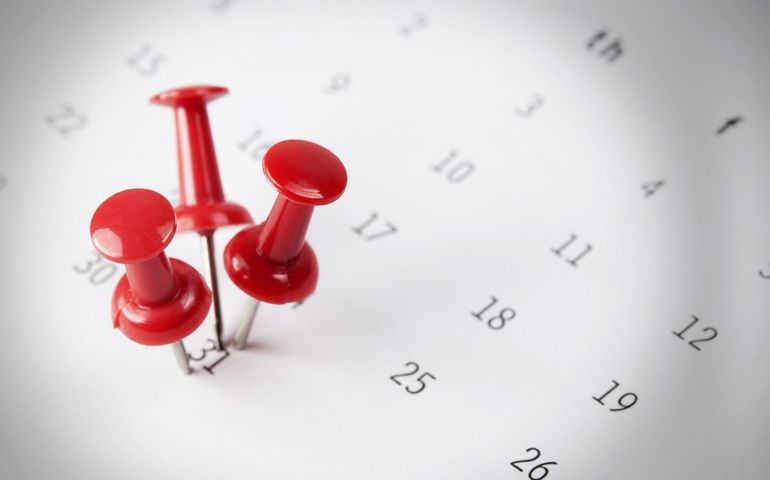 Pushpins with bright light focused on calendar detail, Important date, business trip, or meeting appointment reminder concept image with selective focus