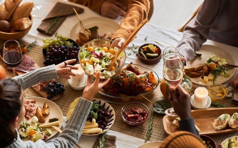 Multiethnic group of people at festive dinner table celebrating Thanksgiving together and enjoying rustic roasted dishes, copy space