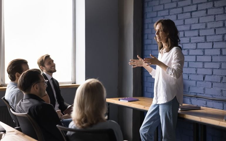 Attractive young company speaker talk to different ages employee on business meeting, help defines task and corporate goal.