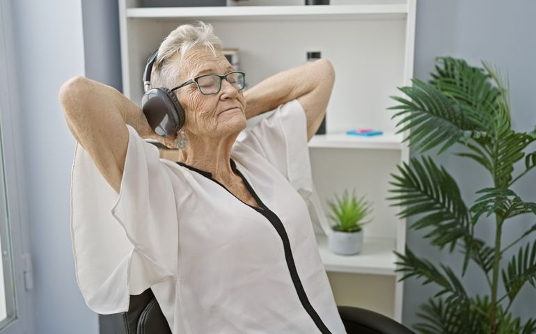 Short-haired, glasses-wearing senior woman boss chilling out in the office, her hands on head, feeling the music through her headphones. the professional boss's downtime.