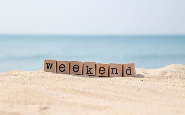 Weekend word on wood rubber stamps stack on the sand beach for vacation and summer season concept, beautiful ocean view during daytime on a sunny day with blue sky on background