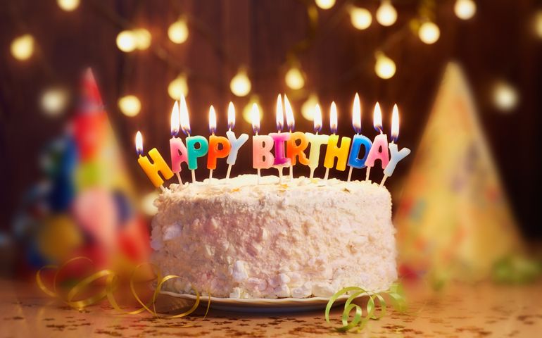 Birthday cake with candles, bright lights bokeh.