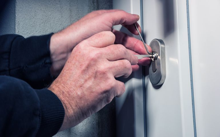 Burglar with lock picking tools breaking and entering into a house