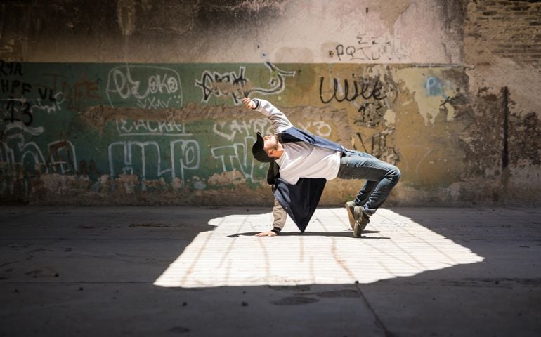 Wide view of a male breakdancer showing off some of his dance moves in an abandoned building