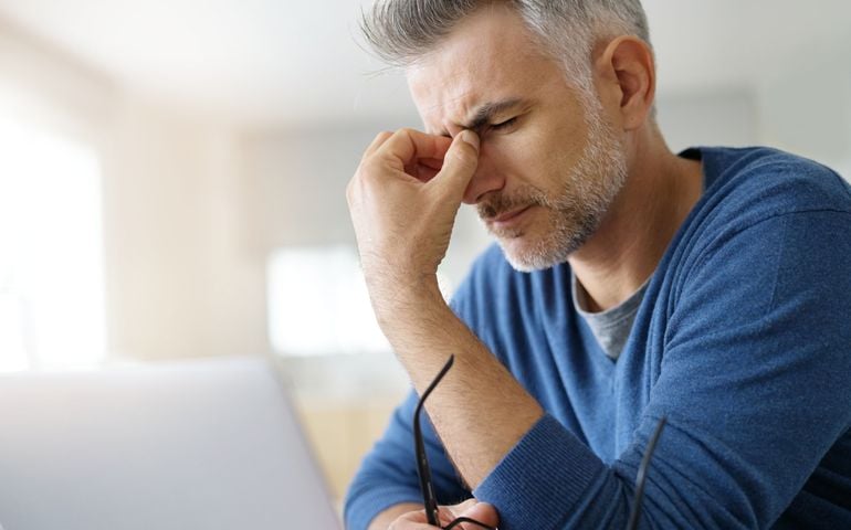 Man at home having a headache in front of laptop