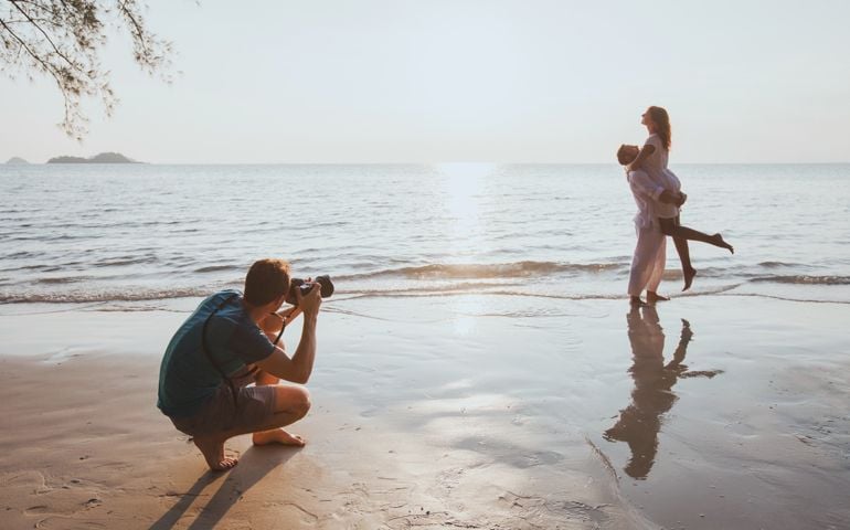 wedding and lifestyle photographer taking photos of affectionate couple on the beach at sunset