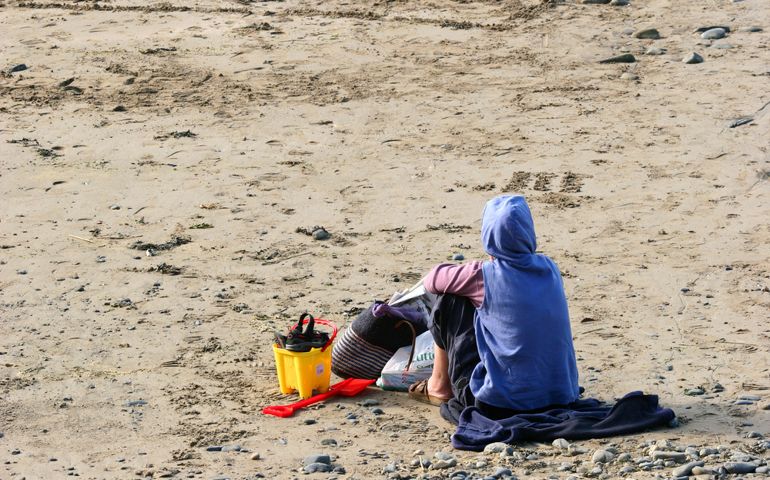 A person fully dressed sitting alone on a beach.