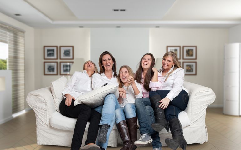 A group of five happy women of different ages laughing in the living room