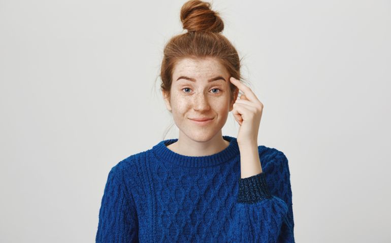 Suggest you sometimes use brains. Indoor shot of attractive redhead woman staring with contempt, holding index finger near temple, telling guy to think before acting stupidly, standing over gray wall