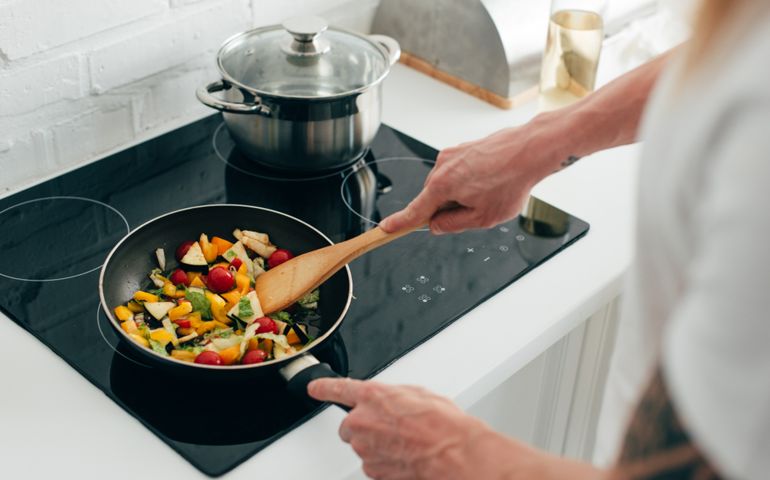 cropped shot of man cooking vegetables in frying pan on electric stove