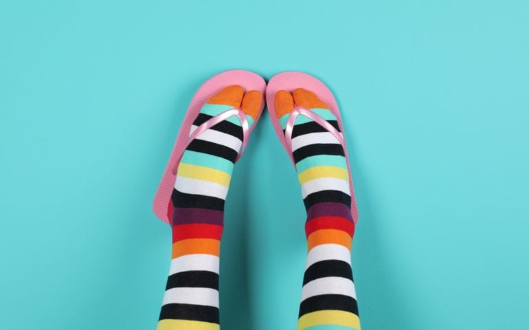 Woman wearing bright socks with flip-flops on color background