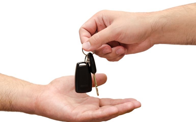 Male hand holding a car key and handing it over to another person isolated