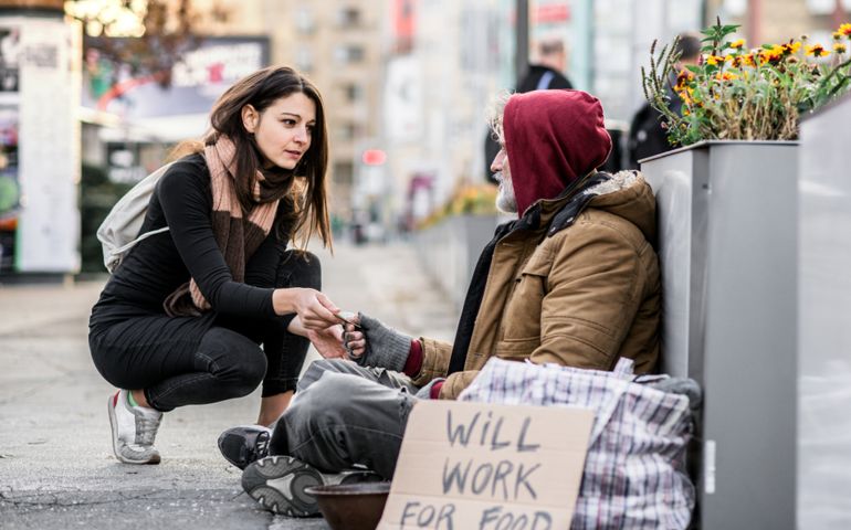 Young woman giving money to homeless beggar man sitting in city.