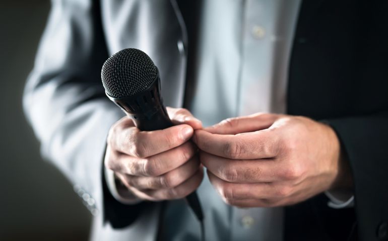 Stage fright concept. Nervous and shy public speaker with microphone. Business man afraid of giving speech for crowd of people or audience. Sweaty hands holding mic. Bad presentation. Stressed singer.