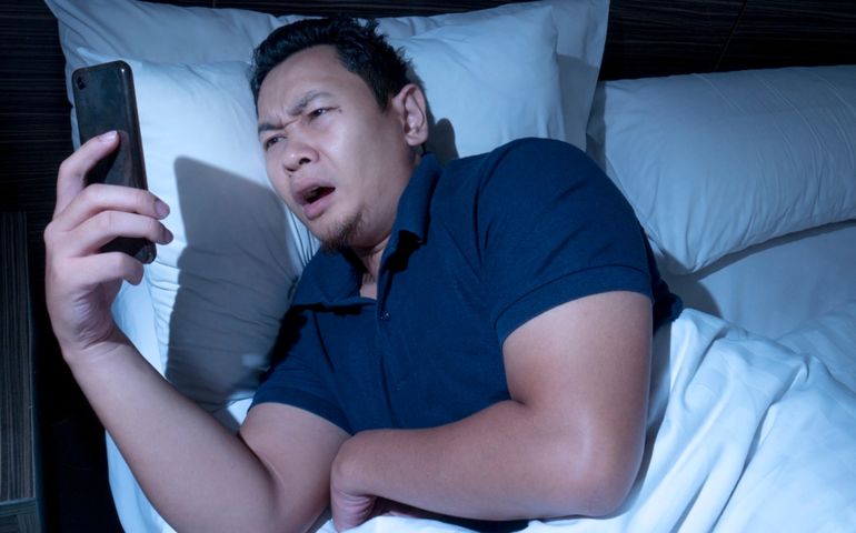 Receiving bad news on phone at midnight concept, Asian male shocked annoyed expression to have bad news on phone while lying on bed at midnight