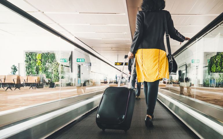 Woman traveller with travel suitcase or luggage walking in airport terminal walkway for vacation travel abroad. concept of travel around world, tourism. Brunette in yellow skirt goes on escalator.