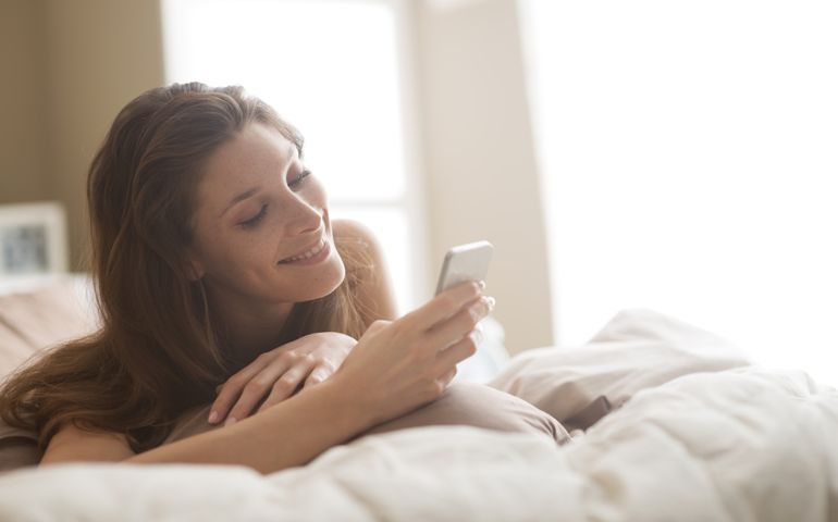 Relaxed woman at home reading a text message in her bright bedroom