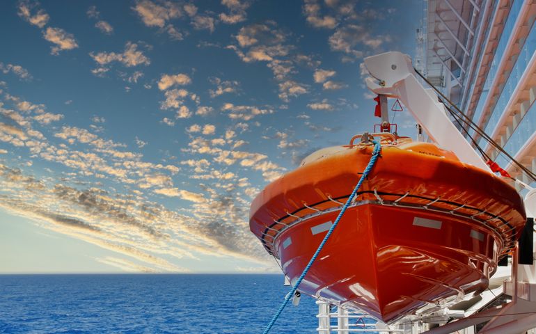 An orange lifeboat hanging over a blue sea on the side of a cruise ship
