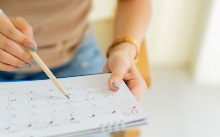 close up on employee woman hand using pen to writing schedule on calendar 2024 to make appointment meeting or manage timetable each day at house for work from home concept