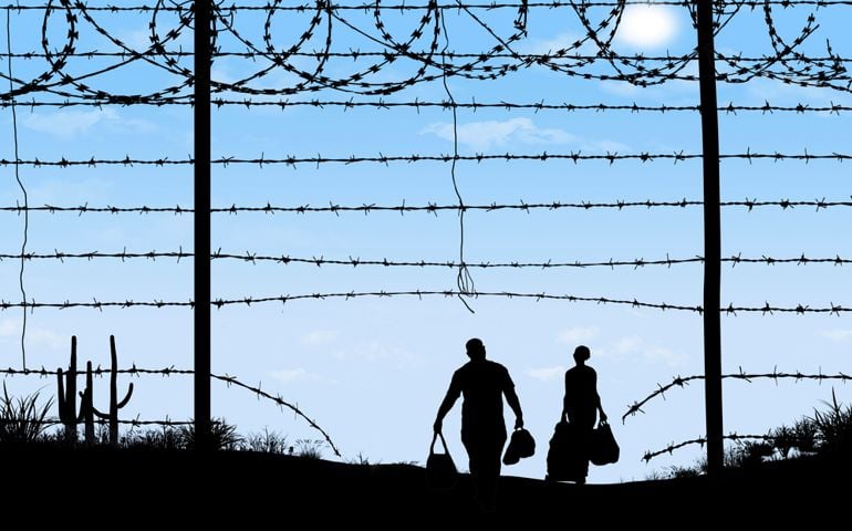 A man and woman are seen in silhouette after breaching a border fence on the southern border of the USA. They have gone through a broken barbed wire fence.