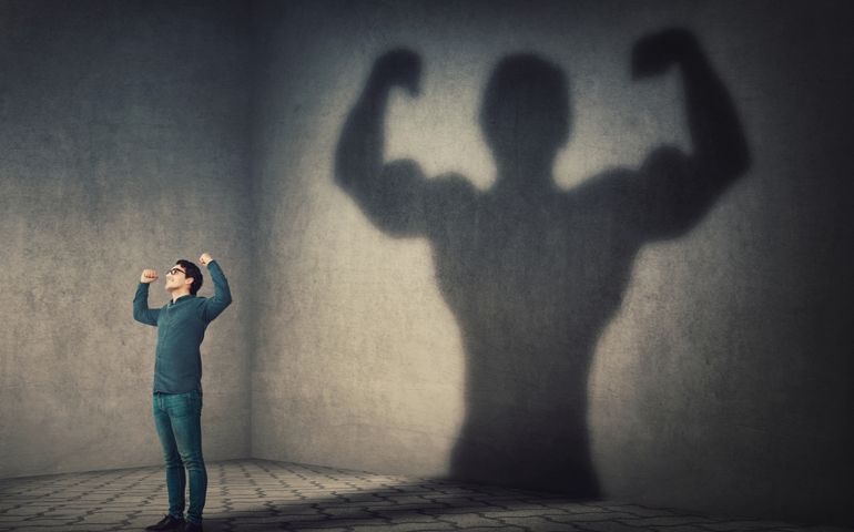Confident man flexing muscles imagine super power as casting a shadow of muscular bodybuilder showing biceps. Strong person facing his fears. Personal development, inner strength, motivation concept.