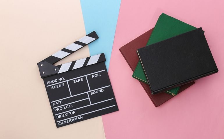 Film clapper board and books on colored pastel background. Movie by book. Cinema industry, entertainment. Top view