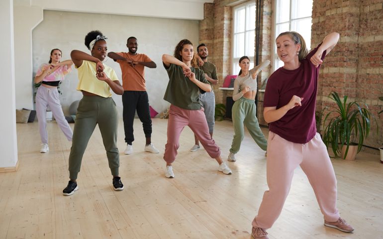 Group of people learning dance exercises with instructor in dance hall