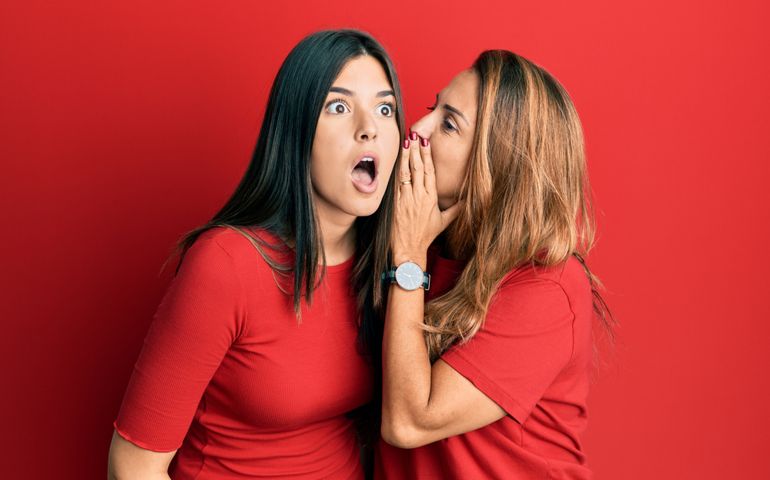Hispanic family of mother and daughter wearing casual clothes over red background hand on mouth telling secret rumor, whispering malicious talk conversation