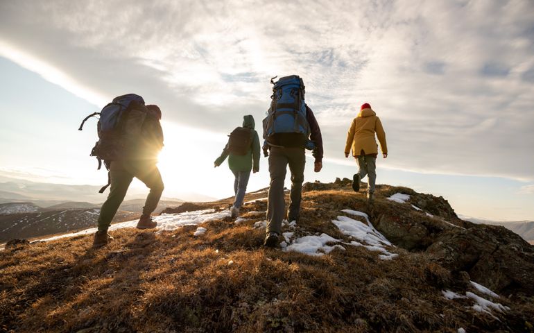 Group of four hikers with backpacks walks in mountains at sunset