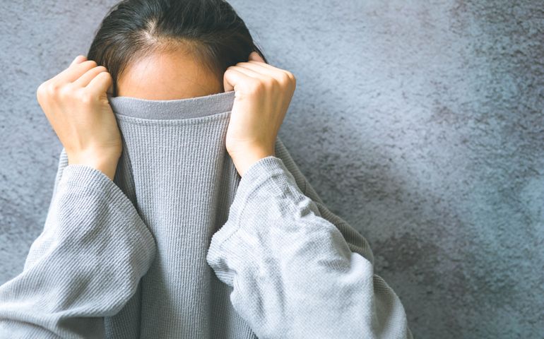 Asian woman hiding face under the clothes. She is pulling a sweater on her head. She has social phobia, trying to be anonymous.