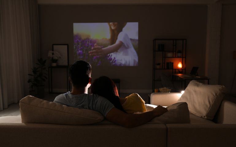 Couple watching movie on sofa at night, back view. Space for text