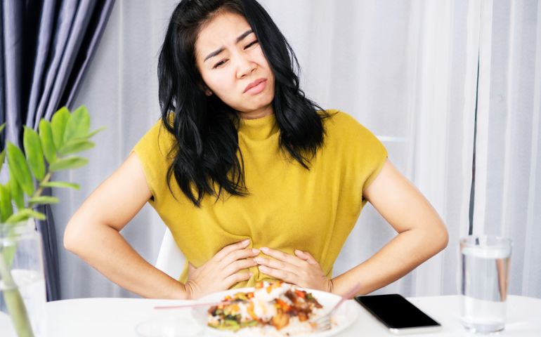 Asian woman suffering from stomachache, GERD after eating spicy food hand holding her pain stomach