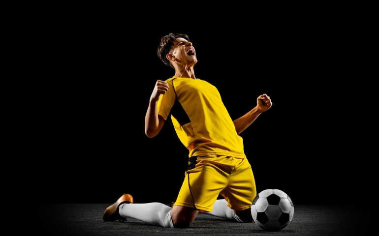 Happy winning pose. Young professional football player in yellow uniform isolated on black background. Sucessful match. Concept of action, team sport game, energy, vitality. Copy space for ad.