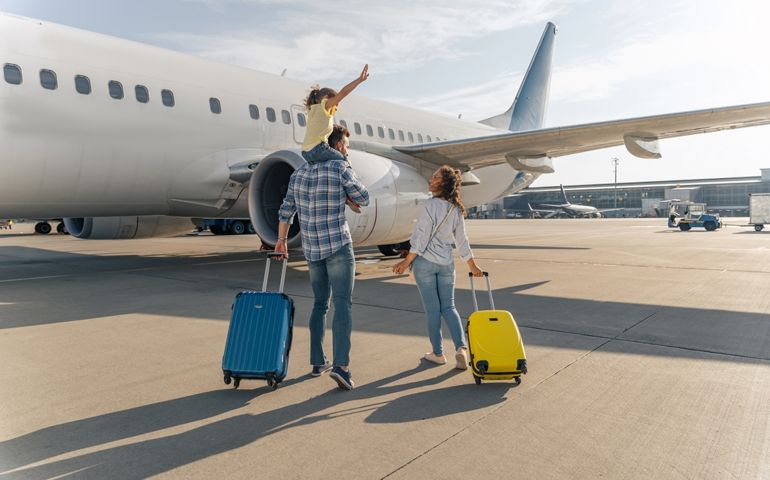 Back view of happy family standing near a large plane with two suitcases outdoor. Trip concept