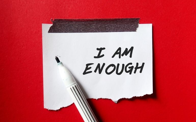 Stick note on red background with pen writing text I AM ENOUGH, Positive mantra affirmation self acceptance, Knowing that you are worthy, valid loved. Embrace all flaws and imperfection