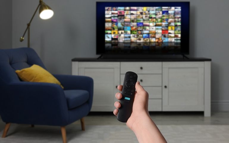 Woman with remote control changing channels while watching TV at home, closeup