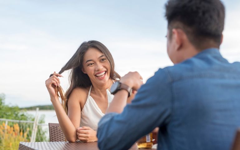 A young woman twirls her hair while listening intently to her date. Interested and attracted to a man she likes. A first date going well. Outdoor cafe scene.