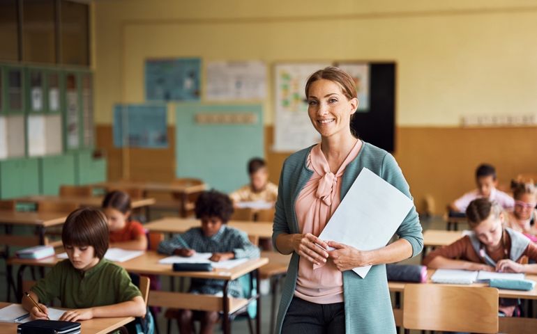 Happy teacher during a class at elementary school looking at camera. Her student are learning in the background.