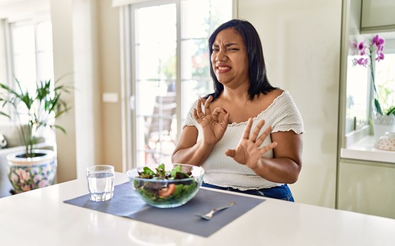Young hispanic woman eating healthy salad at home disgusted expression, displeased and fearful doing disgust face because aversion reaction. with hands raised