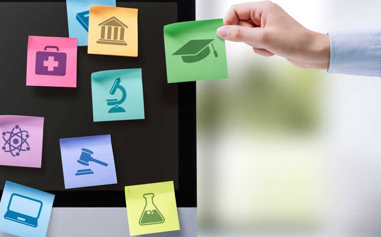 Hand sticking notes with educational subjects icons on a computer screen, online learning concept