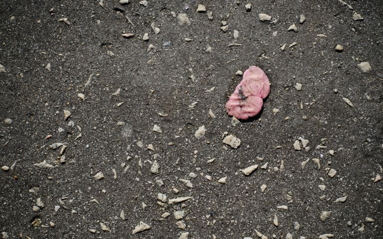 Old pink bubble gum stuck on a dark pavement background