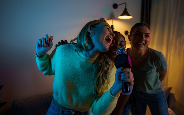 Group of happy friends singing karaoke during a girls night party at the apartment, singing and dancing.
