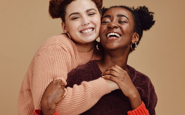 Lesbian, couple hug with young women and happy with fashion and marketing, love and fun together against studio background. Lgbtq community, gen z and freedom with style and lgbt people with pride
