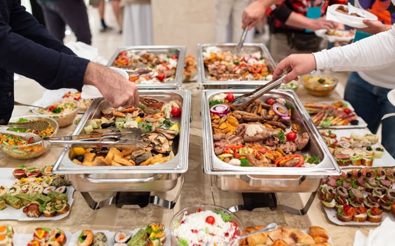 Hands picking up food from buffet catering table at the party.