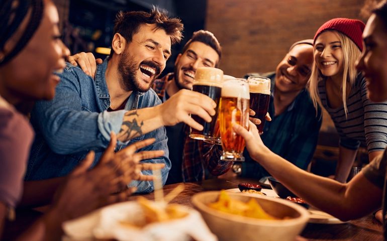 Multiracial group of happy friends having fun while toasting with beer in a bar.
