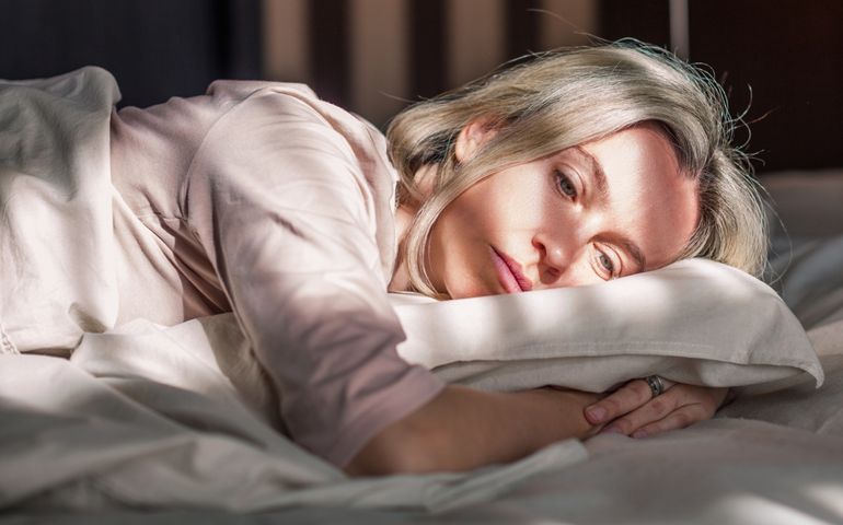 Stressed middle aged woman lying on bed at home and crying