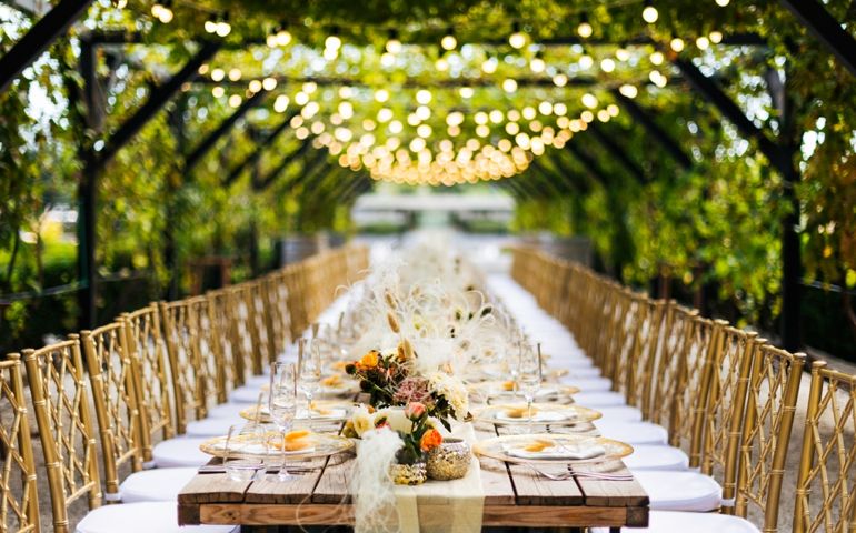 Wedding decorations. Served wedding table with golden plates, golden chairs, napkins, decorative fresh and dried flowers, candles and light bulbs. Celebration details, wedding outdoor